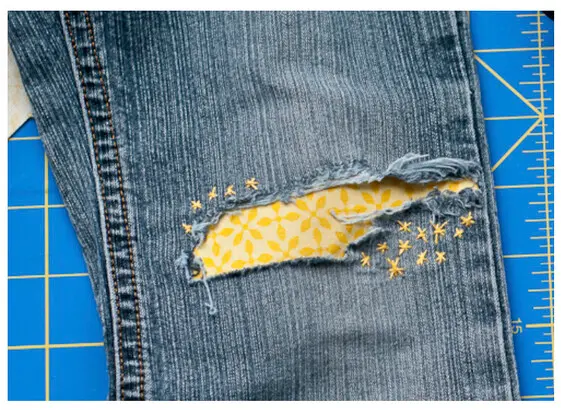 Torn denim jeans patched from the inside with  yellow fabric and decorative stotchingy